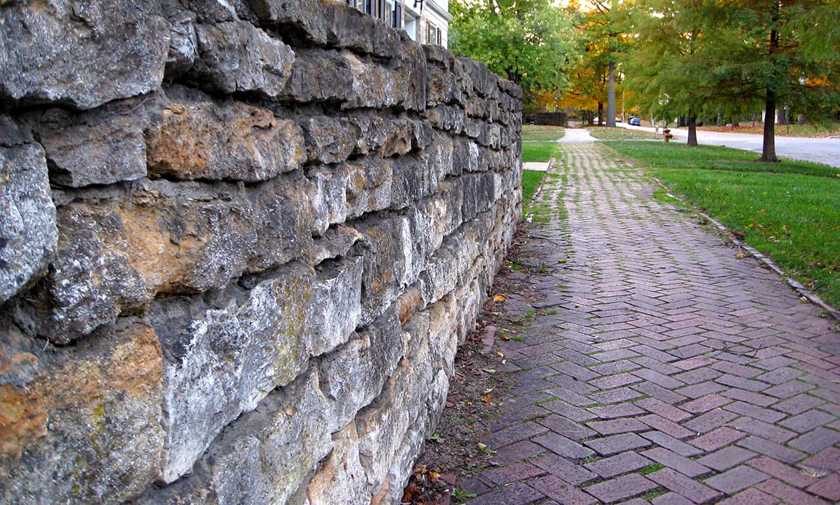 Limestone wall beside a herringbone brick sidewalk in a historic Lawrence, Kansas neighborhood